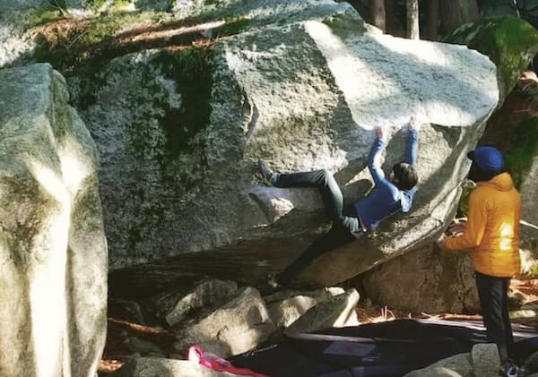 Person climbing up a boulder while being spotted by another person